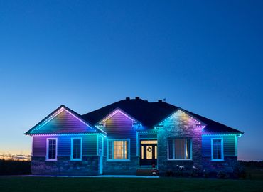 House with colorful LED lights on the roofline during twilight.
