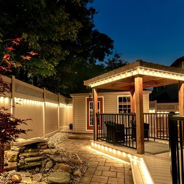 Cozy backyard patio with warm string lights and a small stone water feature at dusk.