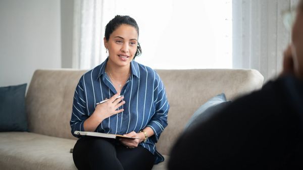 A woman in a striped shirt attentively listens and takes notes during a conversation.