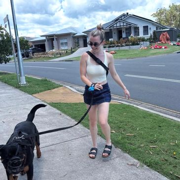 Young woman walking a large dog on a suburban sidewalk.