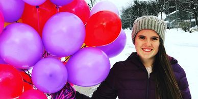 Purple, red and pink balloons with girl in purple coat heading to sweet heart dance. 