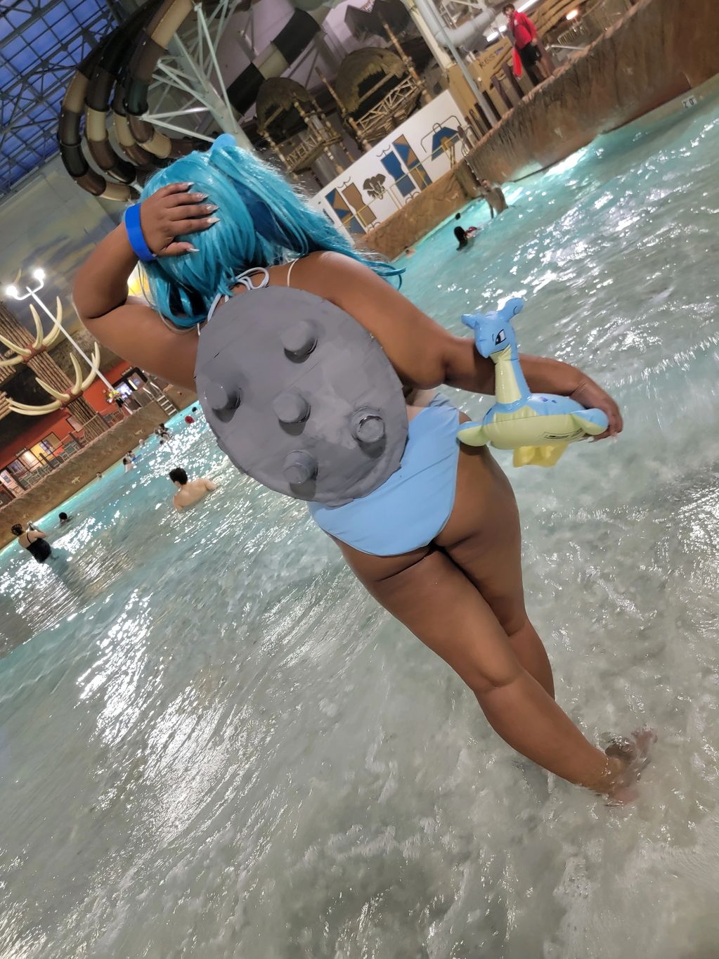 Person in blue wig and shell costume at water park pool.