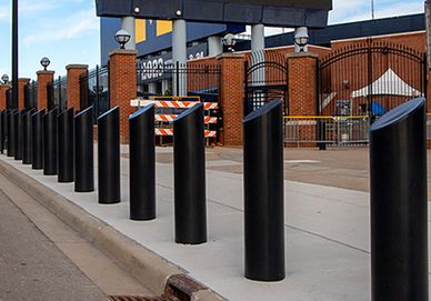 Black bollards lined along a sidewalk near a brick building.