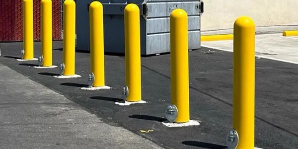Line of yellow bollards near a dumpster.