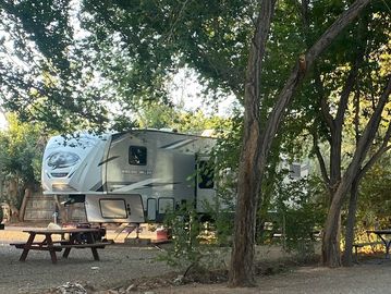 5th wheel camper set up among the shady trees.