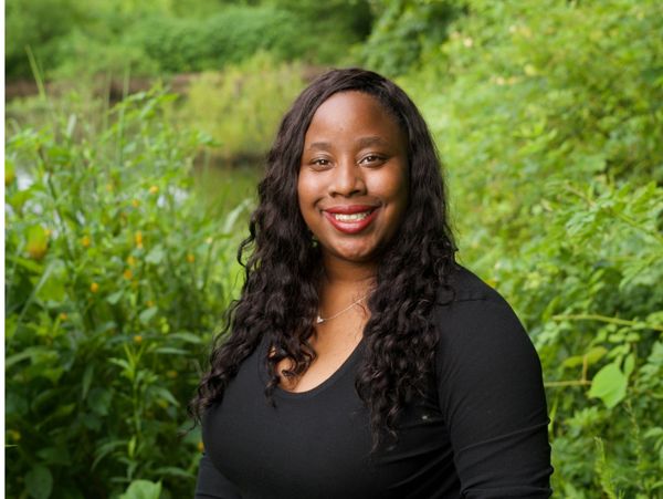 Smiling woman with long curly hair in a black top outdoors.