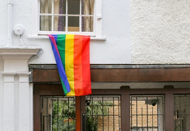 Rainbow pride flag hanging from a window of a white building.