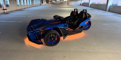 A sleek blue three-wheeled sports car parked in an empty garage.