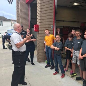 A firefighter talks to a group of children outside a fire station.