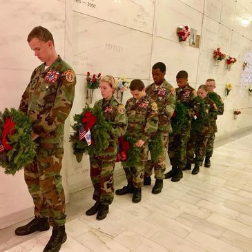 Soldiers in uniform holding wreaths in a solemn memorial ceremony.