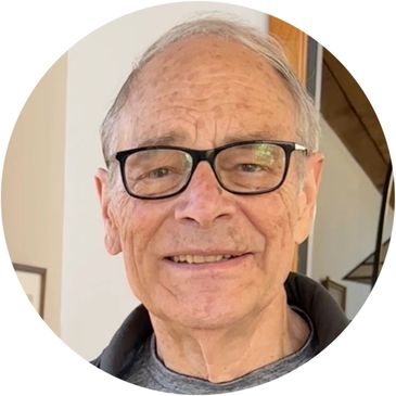 Smiling elderly man with glasses in a casual indoor setting.