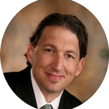 Professional portrait of a man with dark hair and a warm smile.