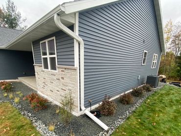 Landscaped garden beds with stones and small shrubs around a blue house.