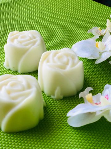 White rose-shaped soaps on a green textured surface with white flower petals.