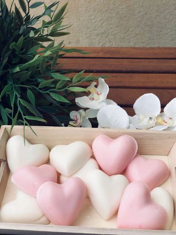 Pink and white heart-shaped soaps in a wooden box with flowers and greenery.