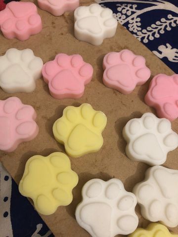 Colorful paw-shaped soaps in pink, white, and yellow on a brown surface.