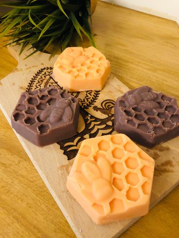 Hexagonal soaps with bee and honeycomb designs on a wooden board.