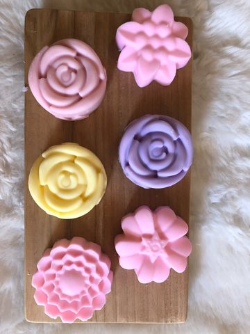 Colorful flower-shaped soaps on a wooden board with a soft white background.