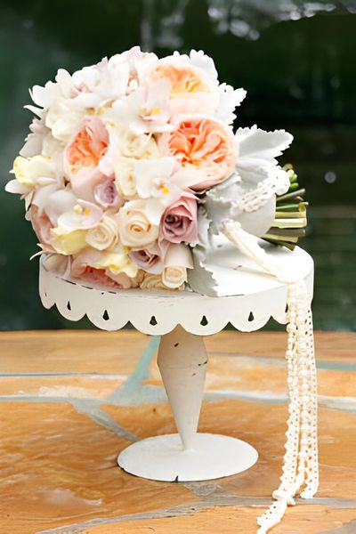 A bridal bouquet with white, pink, and peach flowers, resting on a white stand.