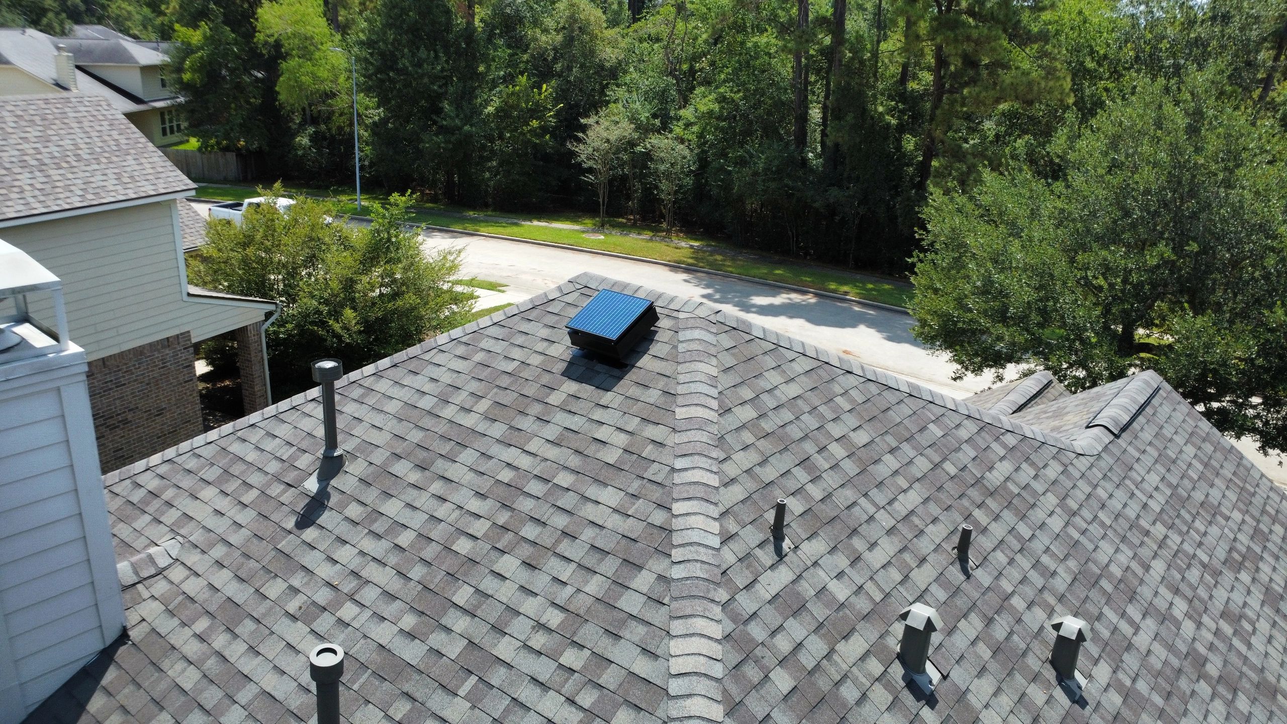 A rooftop with a small solar panel and surrounded by trees.