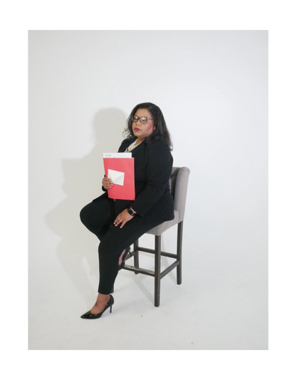 Professional woman in black suit sitting on a stool holding red folder.