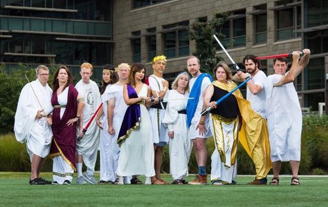 12 people are standing on the soccer fields on Microsoft campus in togas and holding lightsabers. 