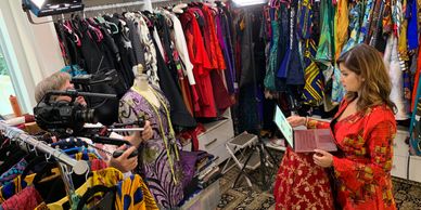 Dona standing in her design studio surrounded by fab fashion and a camera person takes her pic