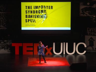 Dona standing on a stage with TEXxUIUC written on it, slides with Imposter Syndrome