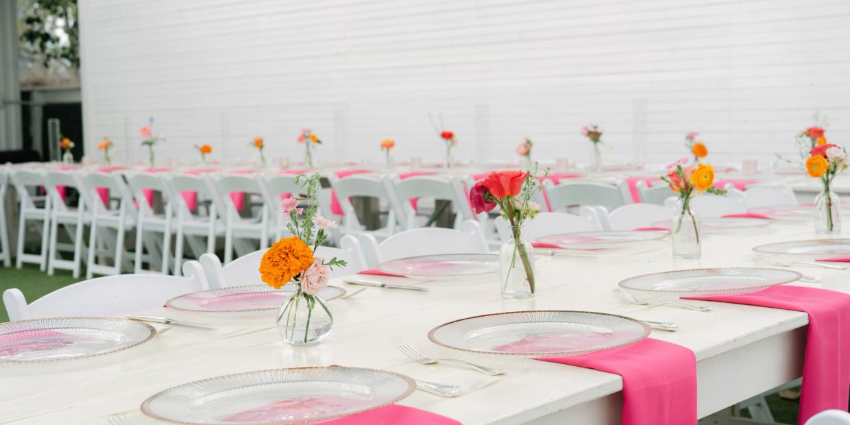 Elegant white tables with pink runners and small floral centerpieces.