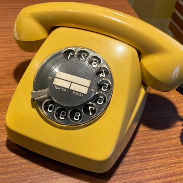 Old yellow rotary phone sitting on a desk.