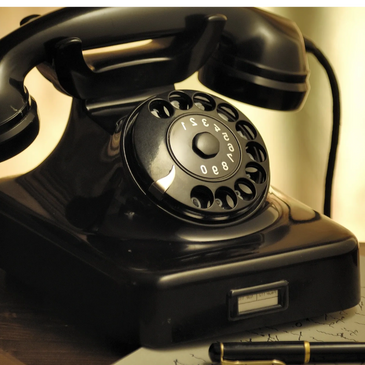 Old black rotary telephone on a desk with a black pen and written letter.