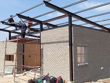 Workers constructing a brick building with steel framework under clear skies.