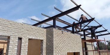 Workers constructing a steel frame roof on a brick building under clear sky.