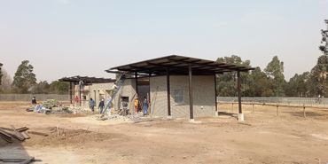 Construction workers building a brick structure with metal roofing in a rural area.