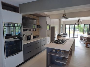 Modern kitchen with island, gas cooktop, and large windows overlooking greenery.