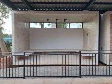 A modern outdoor stage with a white backdrop and black metal railing.