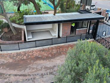 Modern gated security booth with brick and metal design near a sports court.