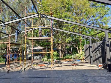 Workers erect a metal framework outdoors on a sunny day.