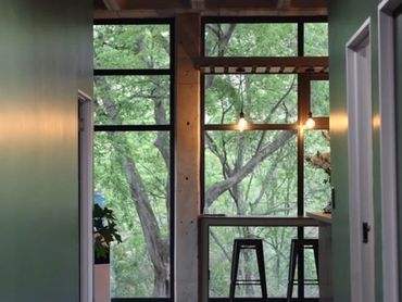 Modern hallway with large windows overlooking green trees and bar stools.