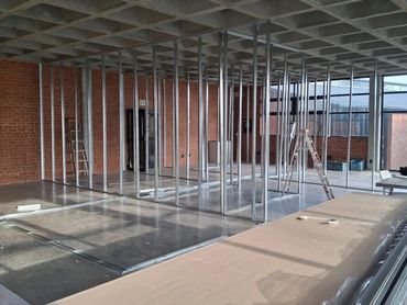 Interior construction with metal framing and brick walls under a grid ceiling.