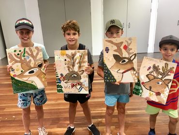 Four boys proudly show their colorful reindeer paintings indoors.