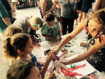 Children and an adult engaged in a lively arts and crafts activity at a crowded event.