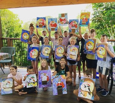 Group of children proudly displaying their colorful holiday-themed paintings outdoors.