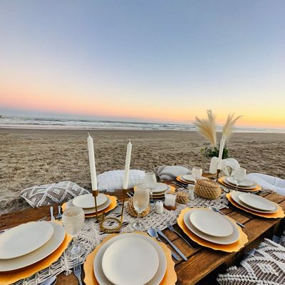 Elegant beachside dinner setup at sunset with rustic decor and candles.