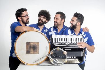 Four musicians in blue shirts holding traditional musical instruments and smiling.