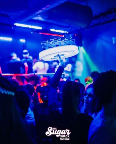 A waiter holds a tray of drinks above a crowded nightclub.