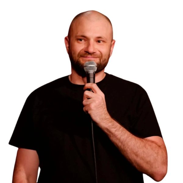 Man in black shirt holding a microphone, smiling.