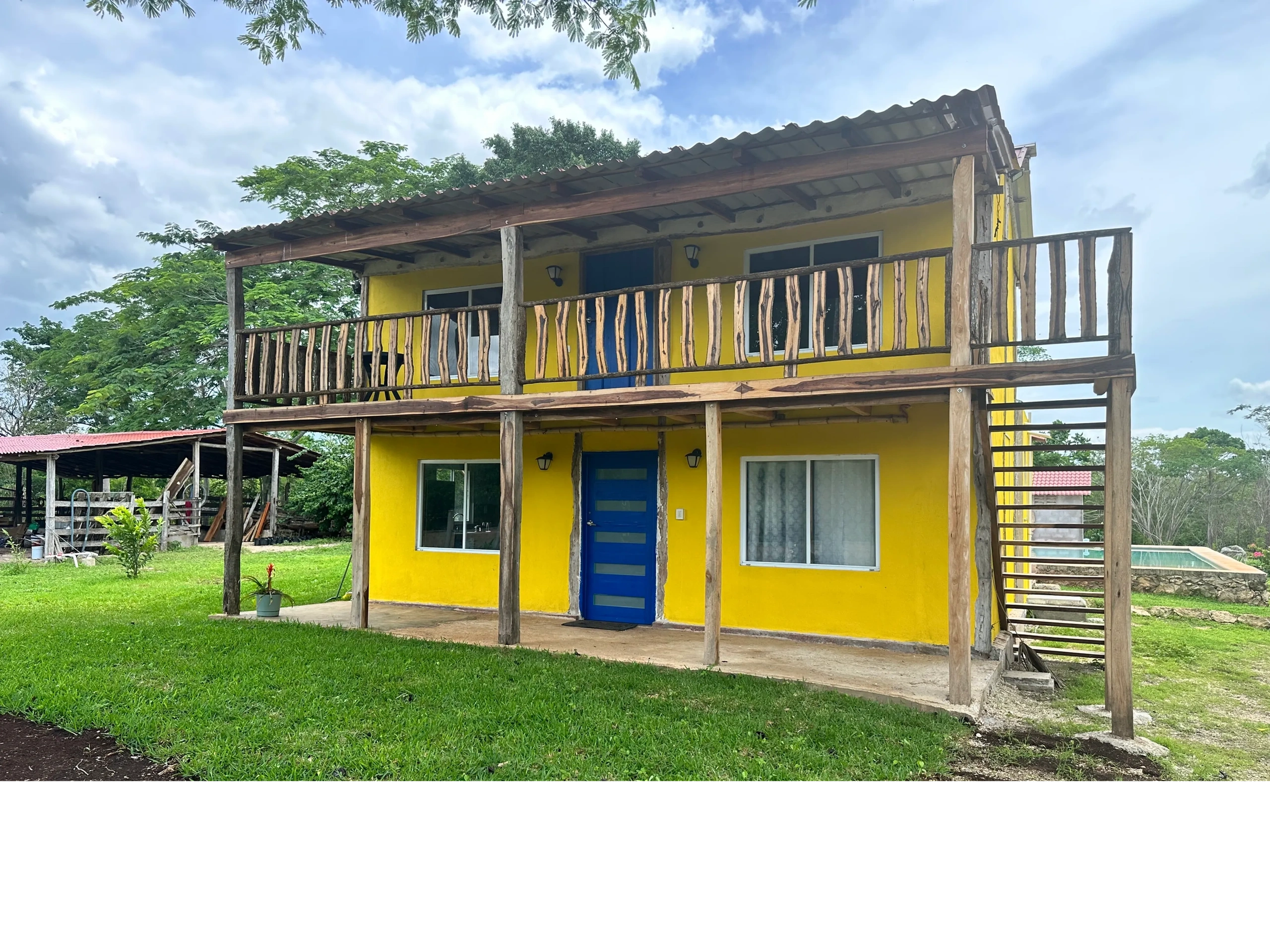 Two-story yellow cabana with rustic wooden balcony and a blue door.