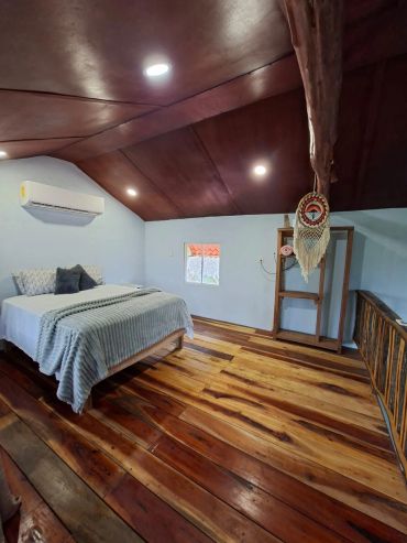 Cozy bedroom with wooden floor and a decorative hanging on the ceiling beam.