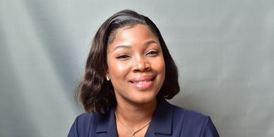 Smiling professional woman in a navy blazer poses against a gray backdrop.
